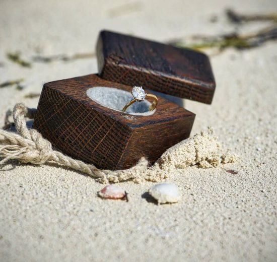 Oval shape diamond engagement ring in wooden box on sand